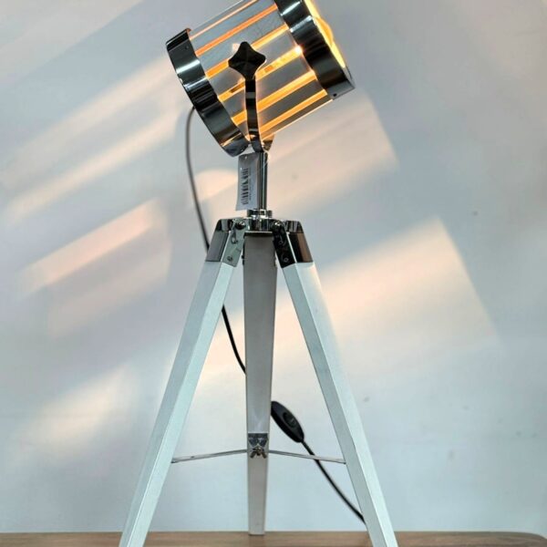 מנורת סטודיו שולחנית דגם 551948199 עם חצובת עץ בצביעה לבנה, גוף תאורה מתכתי בגימור מבריק עם פסי אור פנימיים, ראש מתכוונן לכיוון התאורה, חיבור לחשמל ביתי כולל מפסק. מתאימה לתאורת עבודה ולתאורת אווירה דקורטיבית. גובה: 60 ס״מ